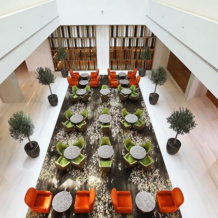 Grand Cosmopolitan Hotel Dubai Luaran gambar The photo showcases a modern interior space, likely a hotel or a lounge. The setting features a large, open area with a stylish arrangement of seating. 

There are vibrant orange and green chairs arranged around circular tables, providing a cozy atmo