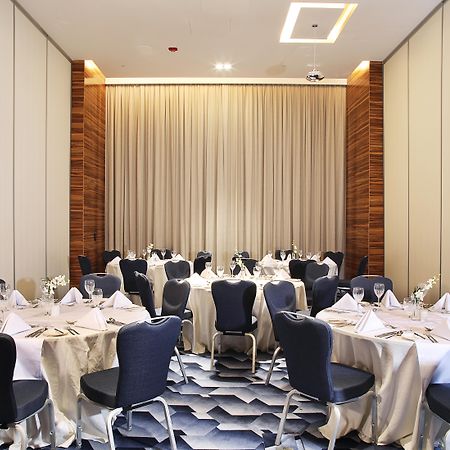 Grand Cosmopolitan Hotel Dubai Luaran gambar The photo shows an elegantly arranged dining area with several round tables. Each table is covered with white tablecloths and set with folded napkins, glassware, and cutlery, indicating that it is prepared for a formal event. The chairs surrounding t