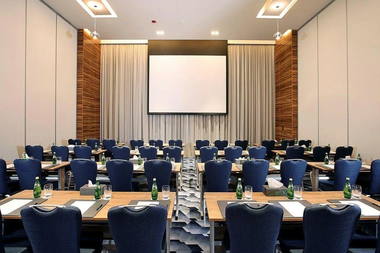 Grand Cosmopolitan Hotel Dubai Luaran gambar The photo shows a conference room set up for a meeting or presentation. There are several rows of tables arranged in a classroom style, each equipped with blue chairs. On each table, there are notepads and pens, and bottles of water are available for