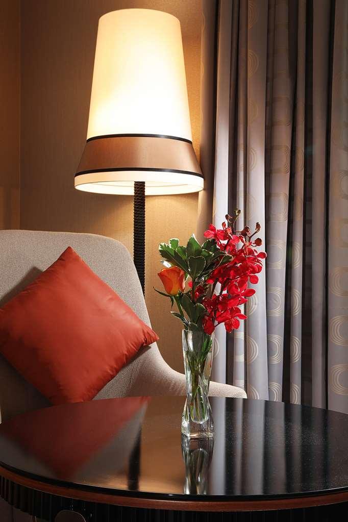 Grand Cosmopolitan Hotel Dubai Bilik gambar The photo shows a cozy corner with a modern armchair that has a light gray fabric. It features a bright orange decorative pillow on one side. Next to the chair is a stylish lamp with a wide shade that emits a warm light. On a small table beside the c