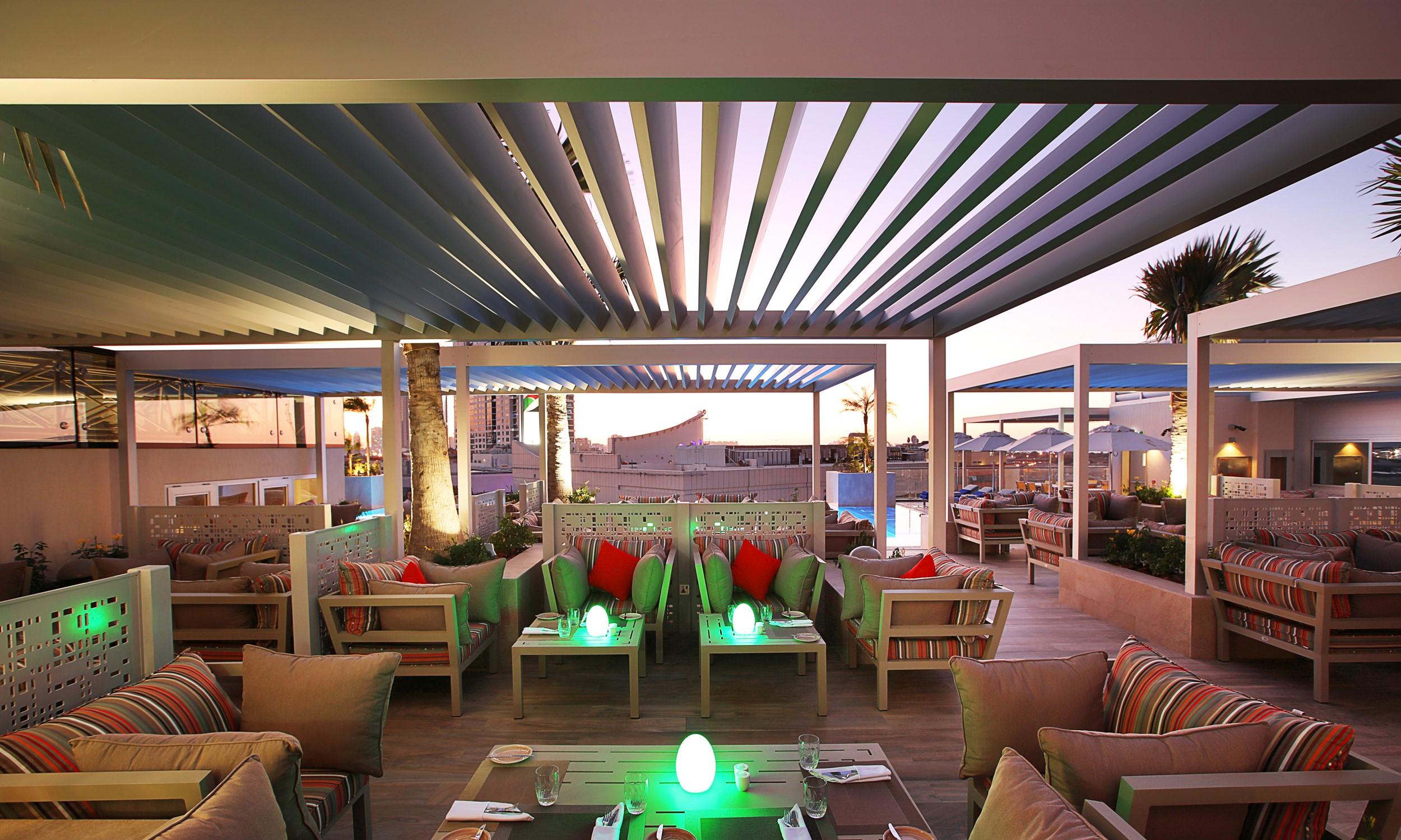 Grand Cosmopolitan Hotel Dubai Luaran gambar The photo depicts a stylish outdoor lounge area, likely located on a rooftop or terrace. The space features modern furnishings with comfortable seating, including sofas and tables. There are colorful cushions accenting the seating, and some tables ha