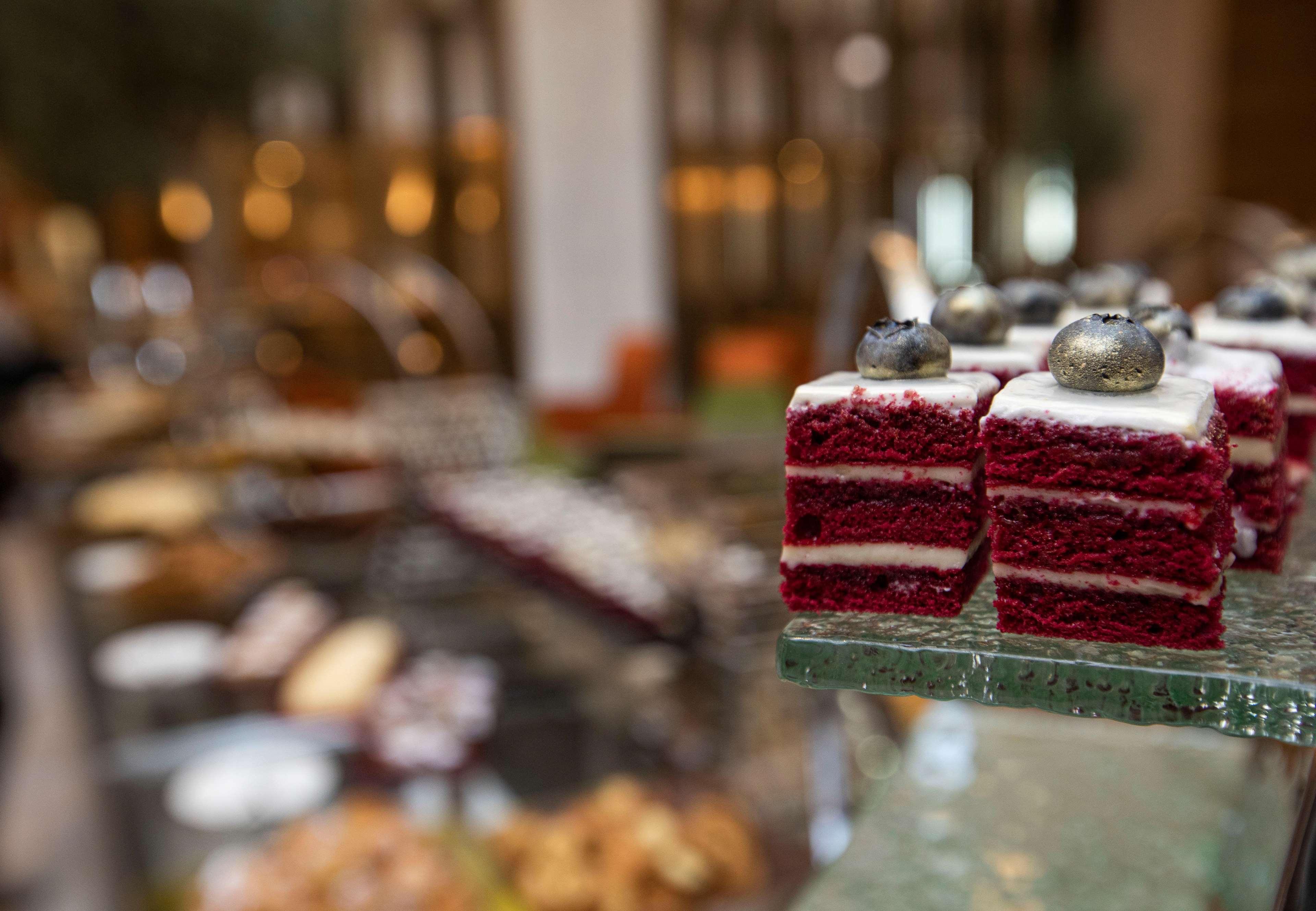 Grand Cosmopolitan Hotel Dubai Luaran gambar The photo showcases a selection of desserts, with a particular focus on red velvet cake squares. The cake pieces are layered, featuring a rich red color and topped with a small decoration. In the background, there are various other desserts and pastr