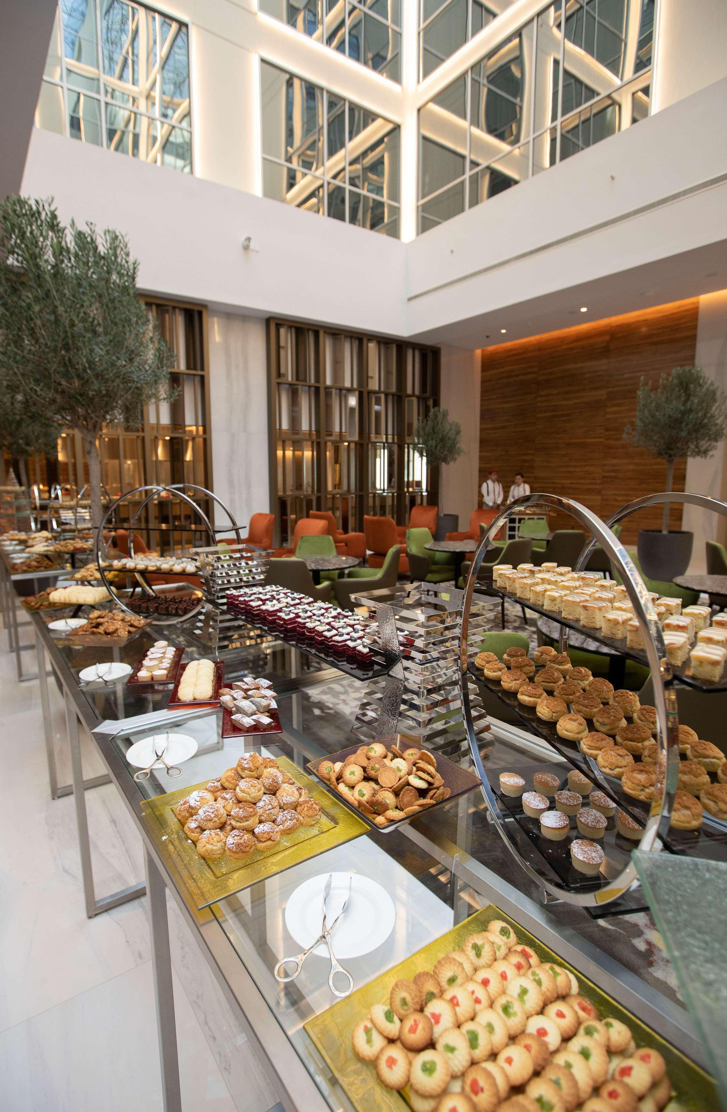 Grand Cosmopolitan Hotel Dubai Luaran gambar The photo depicts a beautifully arranged dessert buffet in a modern setting. Various types of pastries and sweets are displayed on elegant stands and tables. You can see an assortment of items, including cakes, tarts, cookies, and small desserts, app