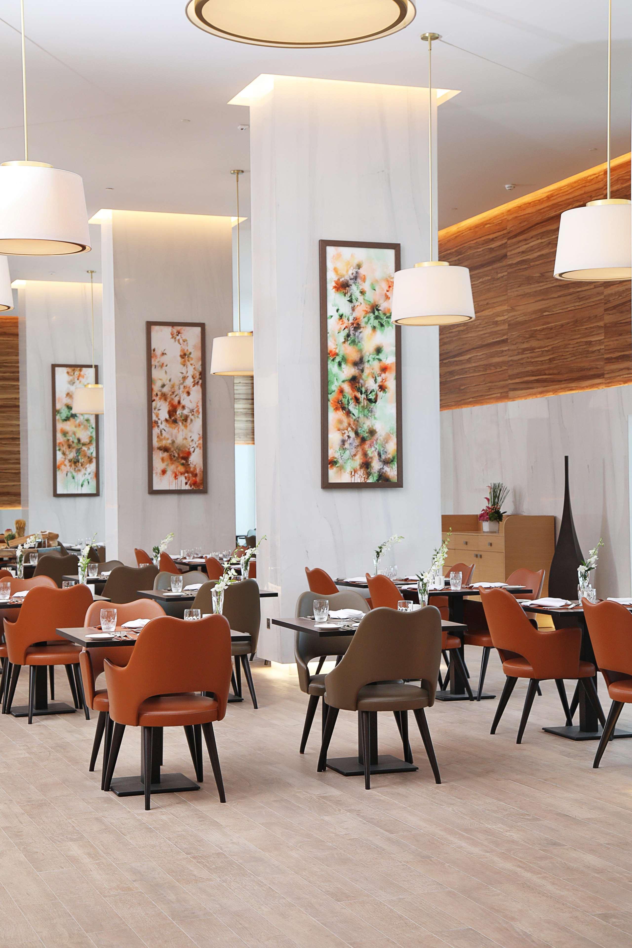 Grand Cosmopolitan Hotel Dubai Luaran gambar The photo shows the interior of a modern restaurant. The space features elegantly set dining tables with glasses and cutlery, and the chairs have a mix of colors, including orange and neutral tones. There are large pieces of artwork on the walls, lik
