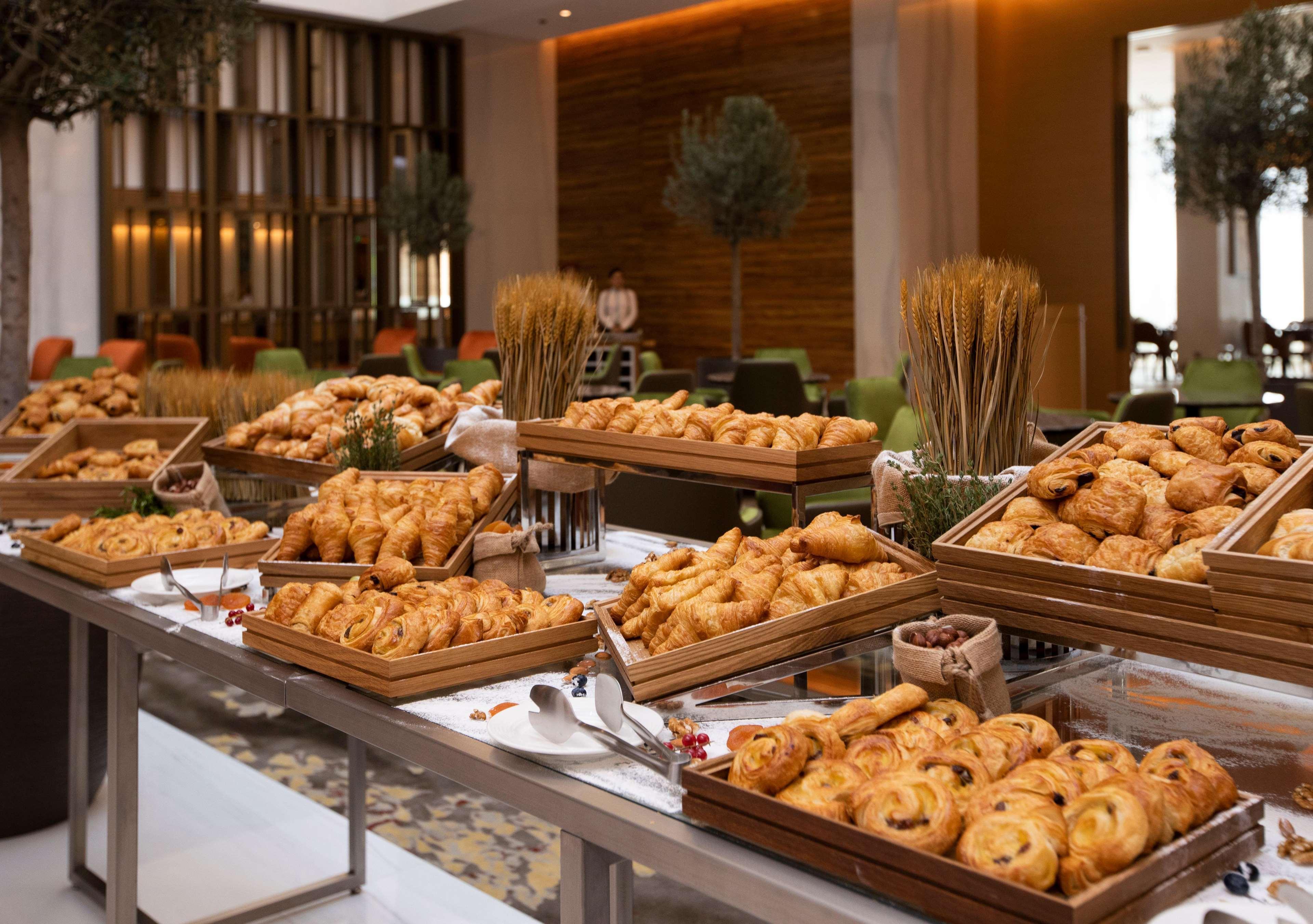 Grand Cosmopolitan Hotel Dubai Luaran gambar The photo shows a lavish spread of baked goods laid out on a table in a buffet setting. There are various trays filled with an assortment of pastries, including croissants, danishes, and other types of bread. The presentation is appealing, with the p