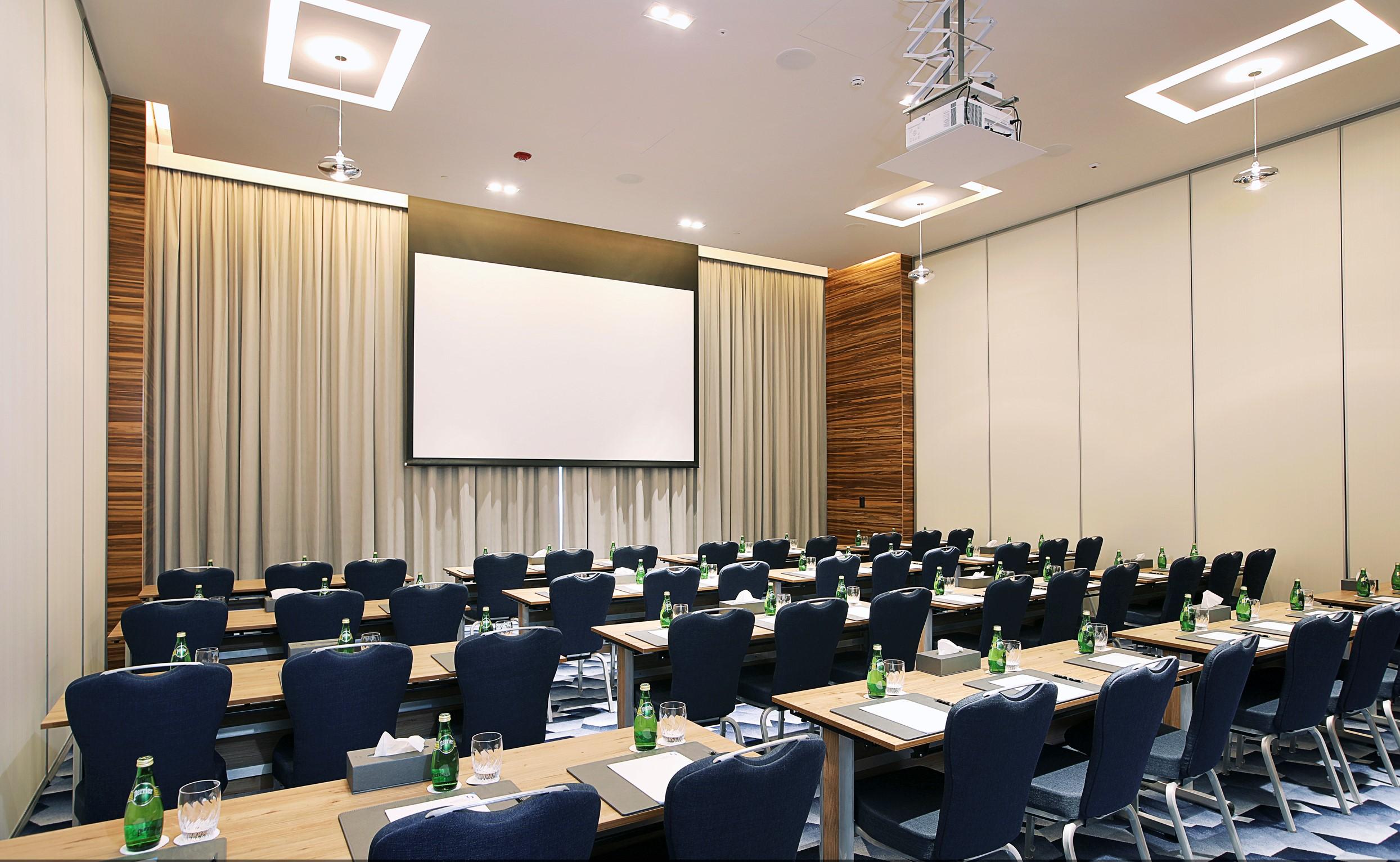 Grand Cosmopolitan Hotel Dubai Luaran gambar The photo shows a conference or meeting room. It features a large screen positioned at the front, likely for presentations. The room is set up with rows of tables and chairs arranged for attendees, with each setting including a notepad and a glass of