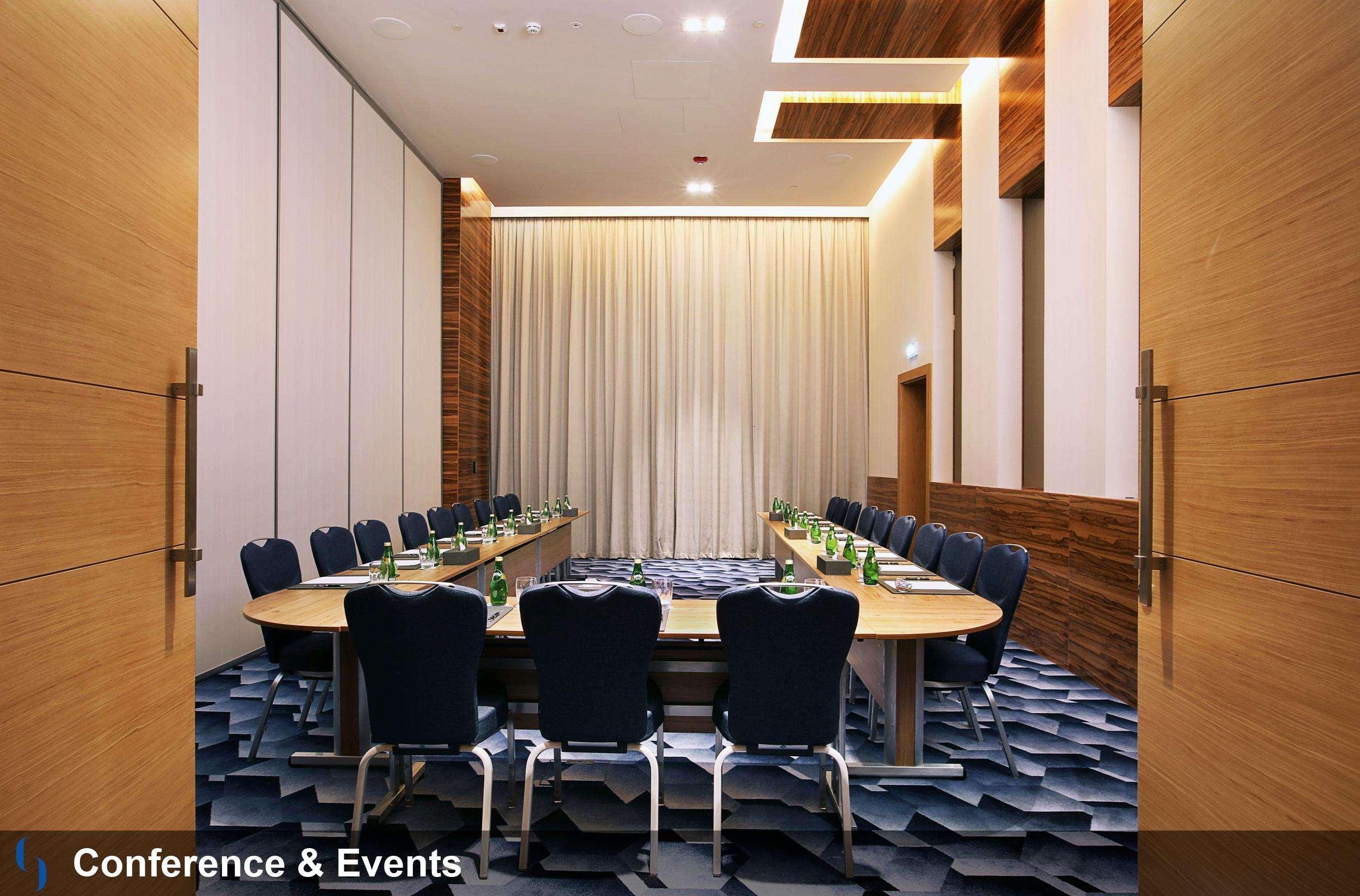 Grand Cosmopolitan Hotel Dubai Luaran gambar The photo shows an elegantly designed conference room. It features a large, rectangular table surrounded by ergonomic chairs, primarily in a dark blue color. The room has wooden accents on the walls, paired with light-colored curtains. The flooring a