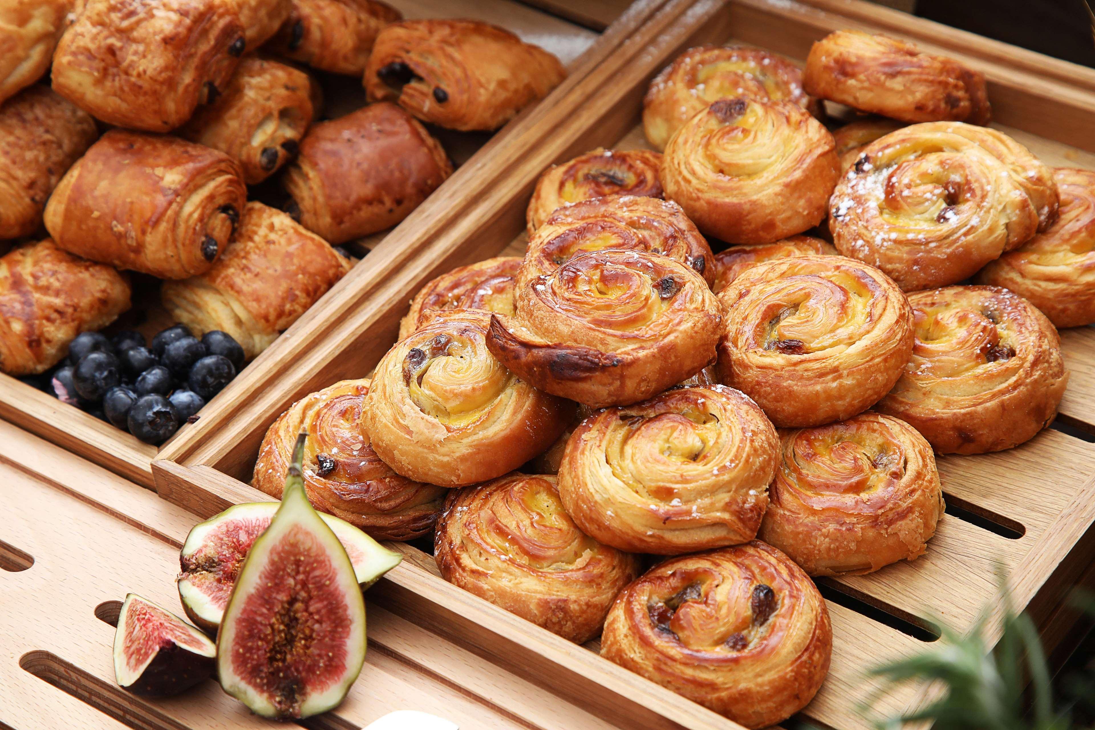 Grand Cosmopolitan Hotel Dubai Luaran gambar The photo showcases a selection of baked goods, primarily featuring various types of pastries. In one wooden tray, there are spiral-shaped pastries, likely danishes or cinnamon rolls, characterized by a golden-brown color and a flaky texture. Some of