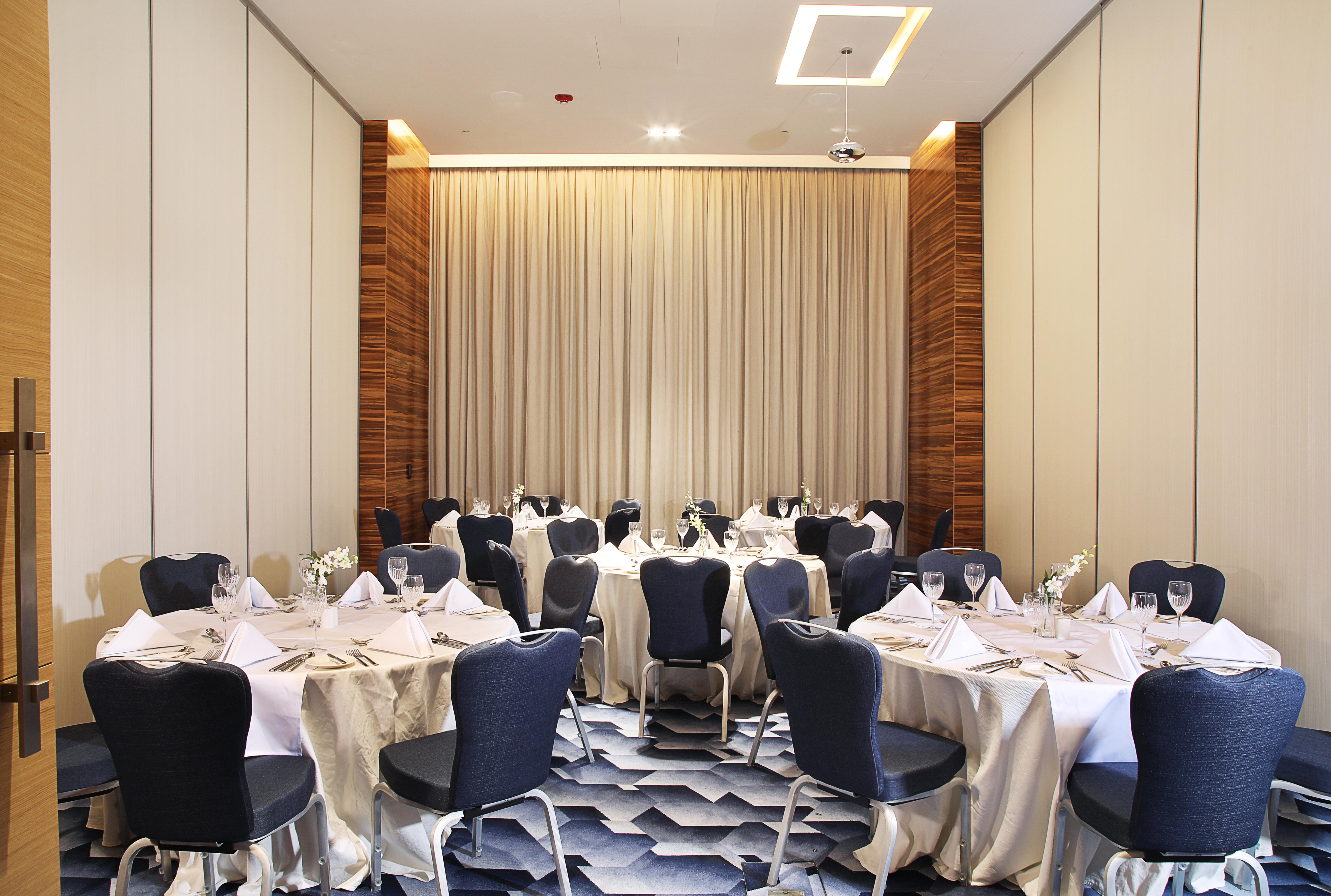Grand Cosmopolitan Hotel Dubai Luaran gambar The photo shows an elegantly arranged dining area with several round tables. Each table is covered with white tablecloths and set with folded napkins, glassware, and cutlery, indicating that it is prepared for a formal event. The chairs surrounding t