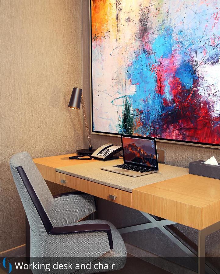 Grand Cosmopolitan Hotel Dubai Luaran gambar The photo depicts a modern workspace. There's a wooden desk with a sleek design, equipped with a laptop open on the surface. Next to the laptop, there is a classic telephone and a small box of tissues. A stylish lamp is positioned on the desk for lig