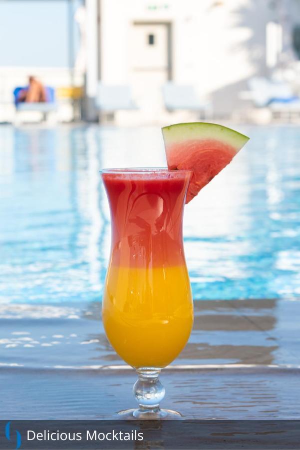 Grand Cosmopolitan Hotel Dubai Luaran gambar The image features a colorful drink in a tall glass. The beverage has a gradient effect, with vibrant red at the top gradually transitioning to a bright yellow at the bottom. A slice of watermelon is perched on the rim of the glass, adding a decorati