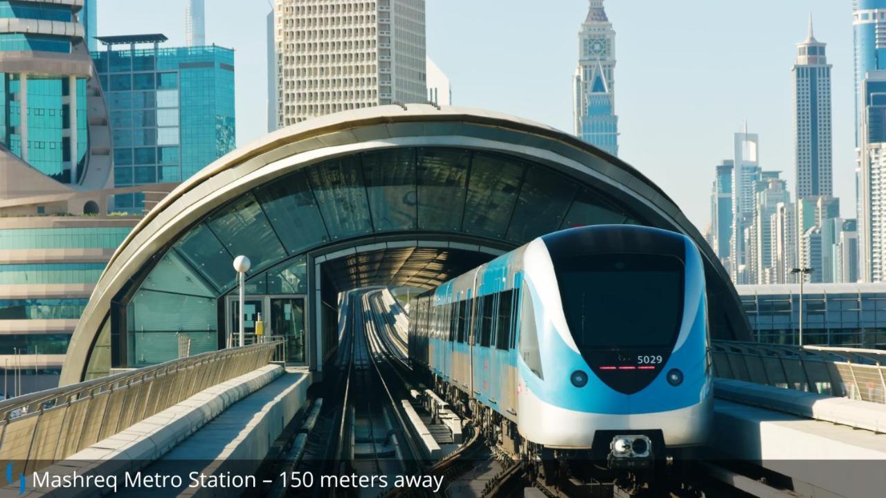 Grand Cosmopolitan Hotel Dubai Luaran gambar The photo shows a modern metro train approaching a station, with a distinctive curved structure overhead that forms part of the station's design. The scene appears to be set in a city with tall skyscrapers in the background, indicating an urban envir