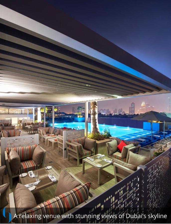 Grand Cosmopolitan Hotel Dubai Luaran gambar The photo depicts a stylish outdoor lounge area at night. It features a modern design with comfortable seating arrangements, including plush sofas and tables under a canopy. In the background, there is a swimming pool illuminated with blue lights, cr