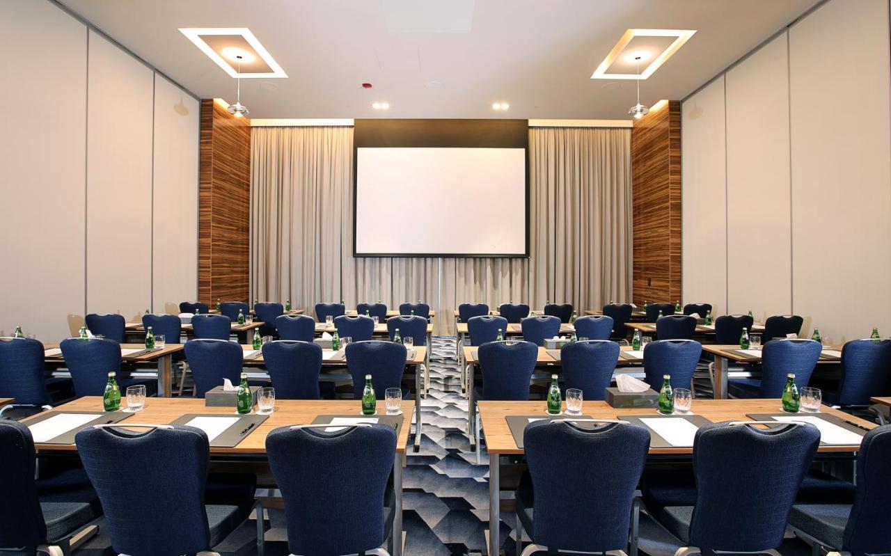 Grand Cosmopolitan Hotel Dubai Luaran gambar The photo shows a conference room set up for a meeting or presentation. There are several rows of tables arranged in a classroom style, each with blue chairs. Each table appears to have a notepad and pen for participants. At the front of the room, th
